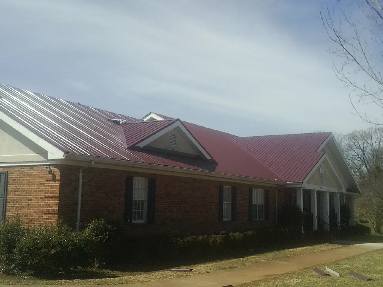 Red metal roof with gabled entries on a long brick building, from a Hail Damage Roof Repair job in Iola
