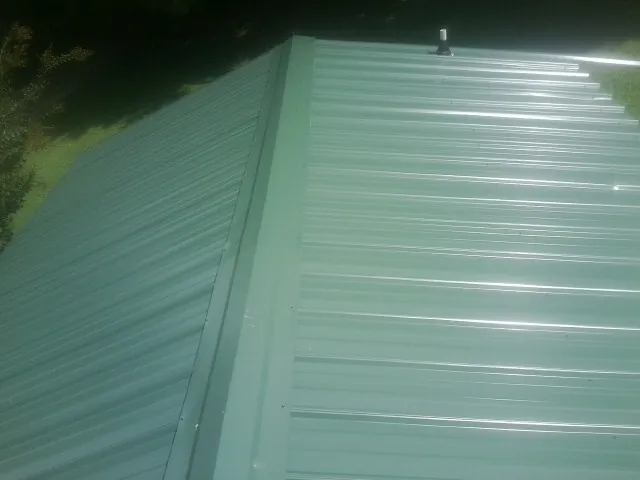 New green metal panels meeting at the ridge of a roof — Flat Roof Repair work by our crew in Iola