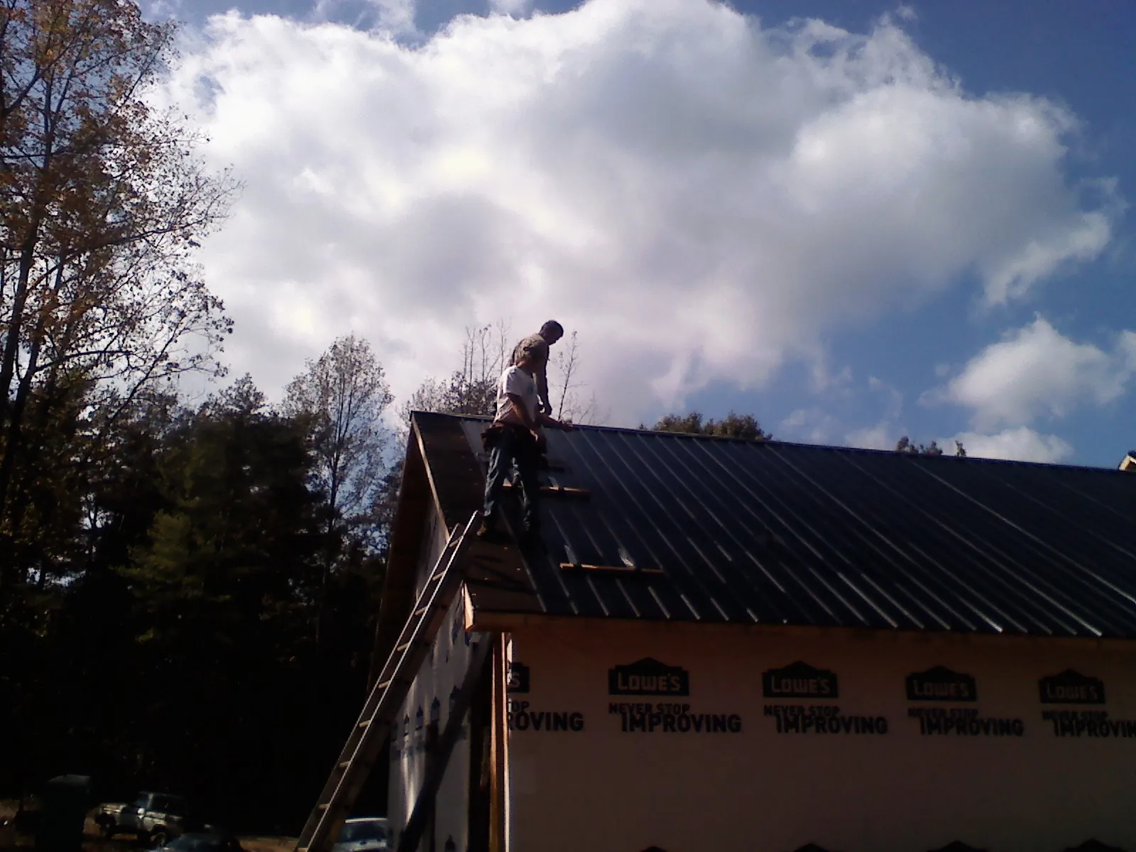 Roofer fastening dark metal panels high against a cloudy sky, from a Roof Inspection job in Iola