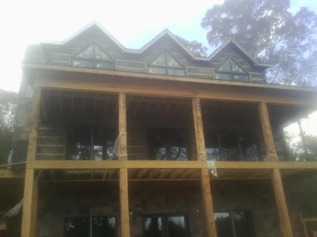 Dormers and porch framing on a large log home under construction — Roof Coating work by our crew in Iola