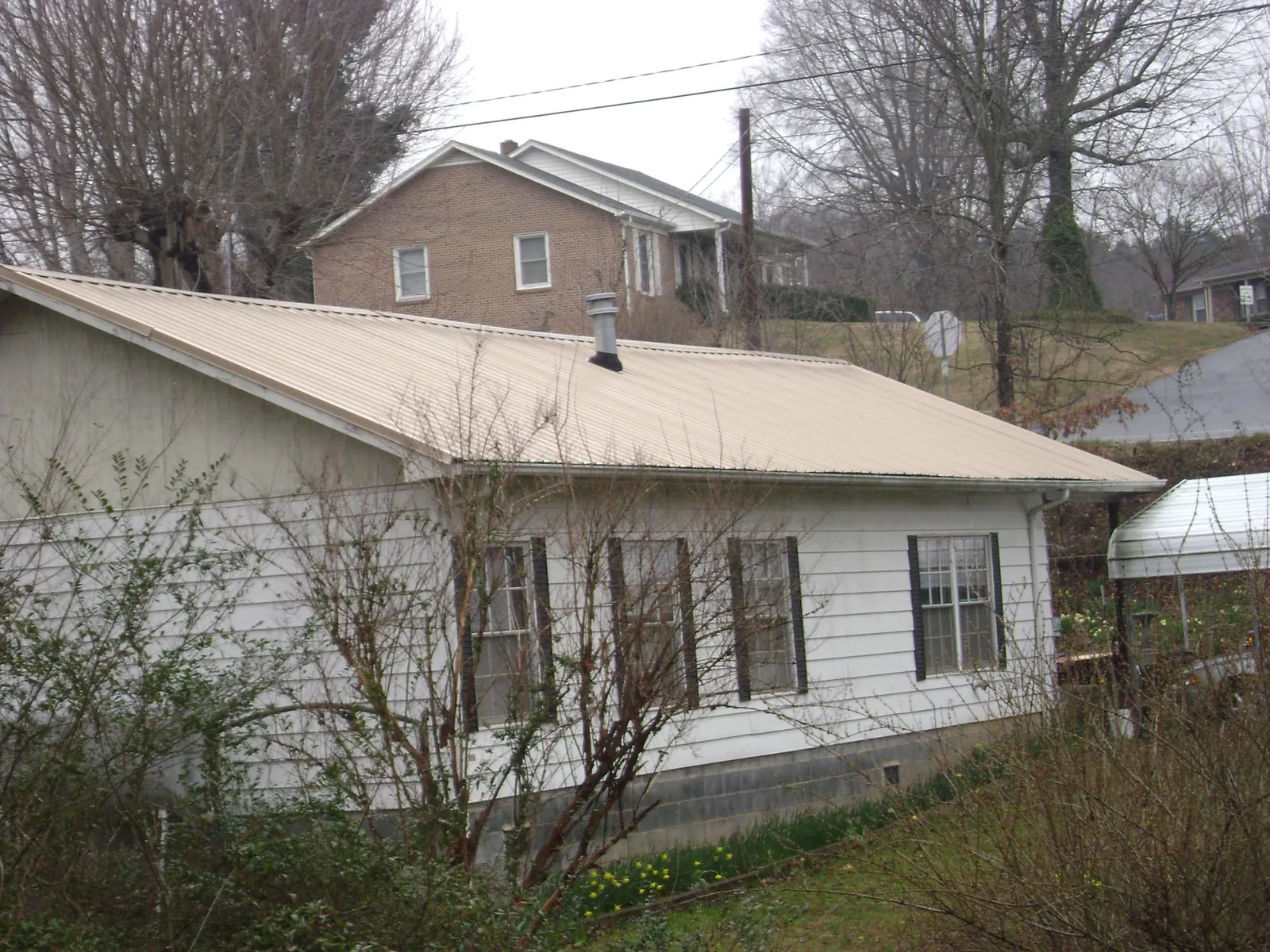 Tan metal roof on a white sided house set into a hillside — Commercial Roofing by Roofing Brothers in Iola